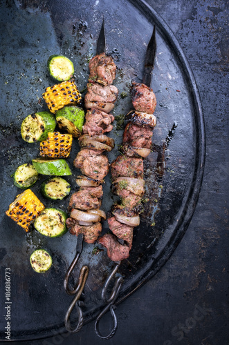 Traditional Russian shashlik on a barbecue skewer with vegetable as top view on old board with copy space right photo