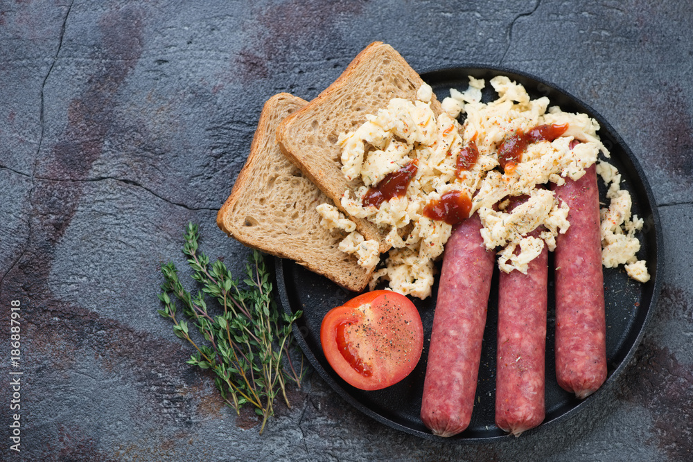 Metal tray with beef sausages and scrambled eggs. Flat-lay with space on a cracked asphalt background, horizontal shot