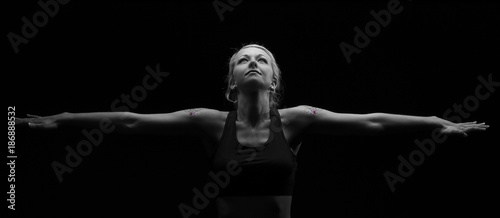 Beautiful fit and healthy blond woman in black top in dark with arms stretched artistic conversion