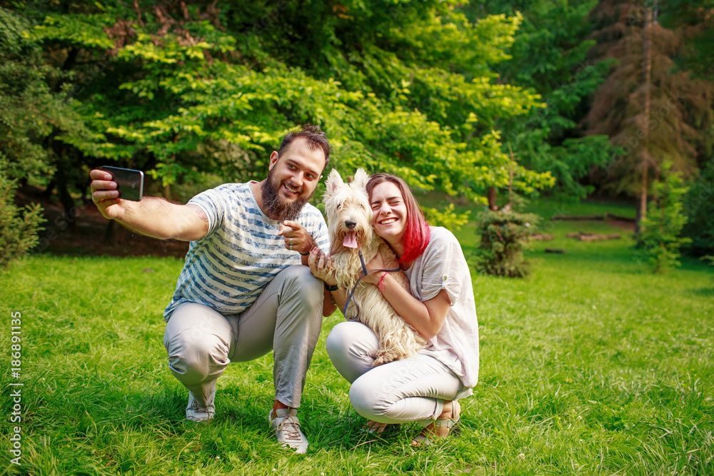 Fototapeta premium Loving couple making selfie with dog in park