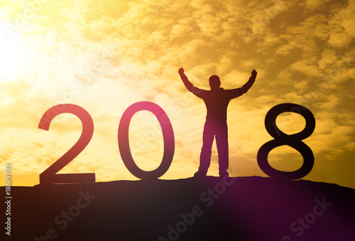 Silhouette of a man hands up on a mountain top and sunlight with text 2018 sign happy new year calendar holiday concept. New Year Christmas