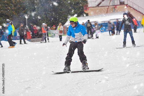 Young man on snowboard downhill with people in the background