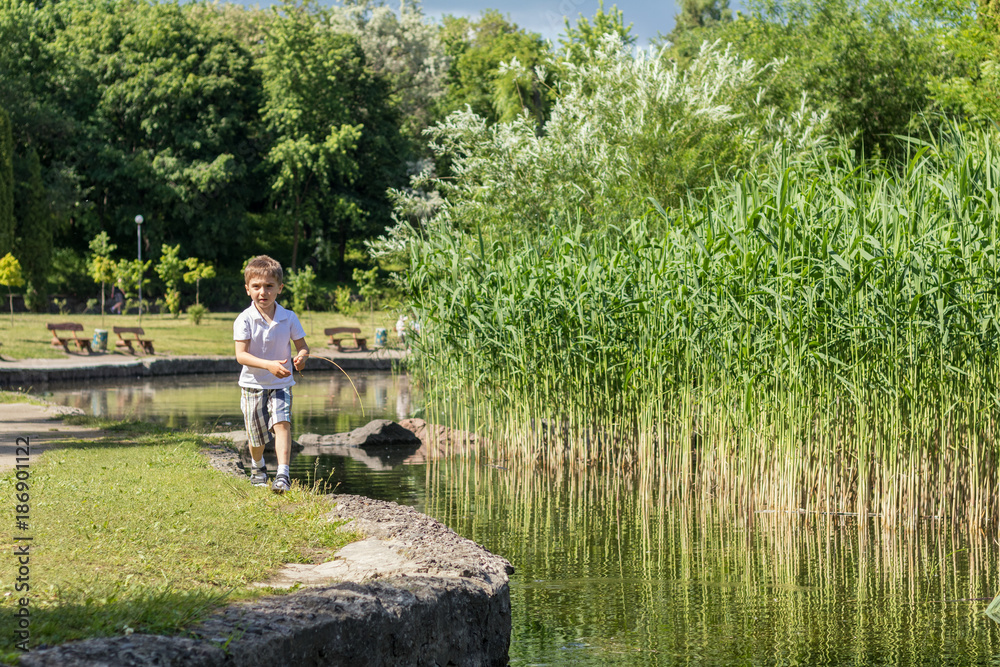 Happy little boy playing at the pond in the city park on a summer sunny day. Close up. Beautiful summer background with copy space Happy little boy playing at the pond in the city park on a summer sunny day. Close up. Beautiful summer background with copy space