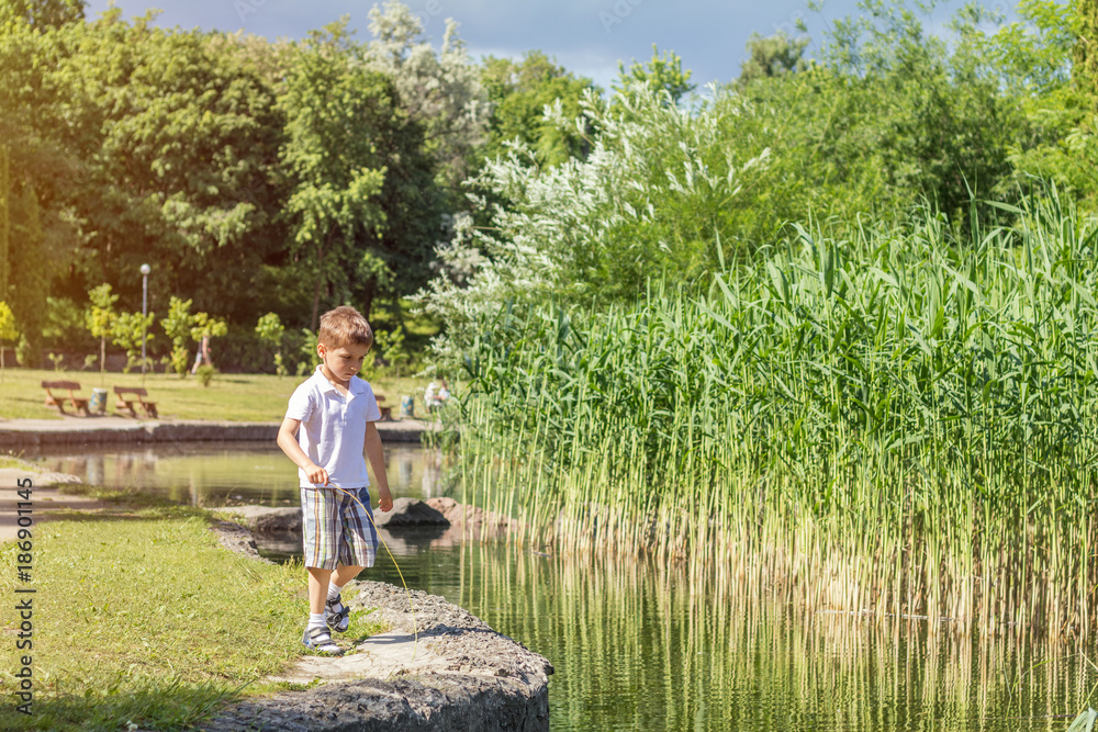 Happy little boy playing at the pond in the city park on a summer sunny day. Close up. Beautiful summer background with copy space Happy little boy playing at the pond in the city park on a summer sunny day. Close up. Beautiful summer background with copy space