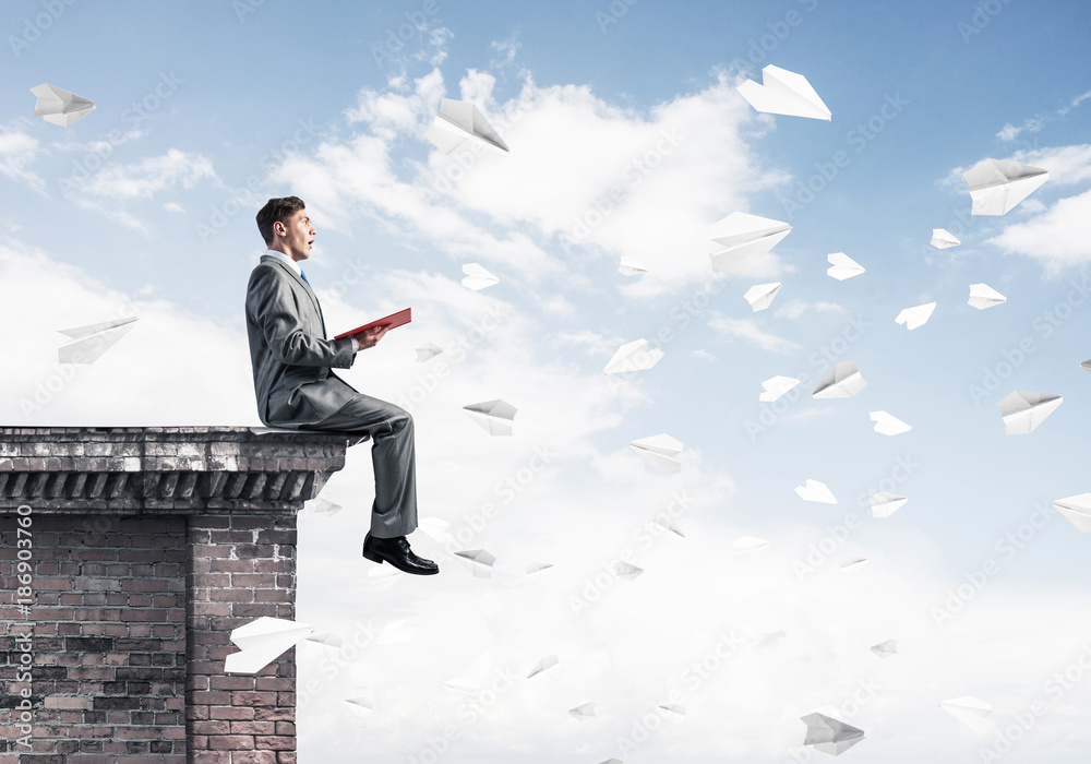 Man on roof edge reading book and cityscape at background Man on roof edge reading book and cityscape at background