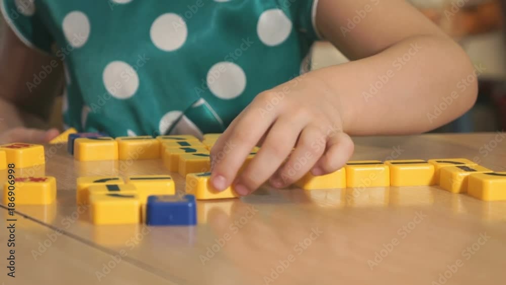 Close-up of unknown little girl in polka dot dress sitting at desk in the kindergarten playing in developing designer and collecting shape in the form of rope on yellow blocks. Close-up of unknown little girl in polka dot dress sitting at desk in the kindergarten playing in developing designer and collecting shape in the form of rope on yellow blocks.