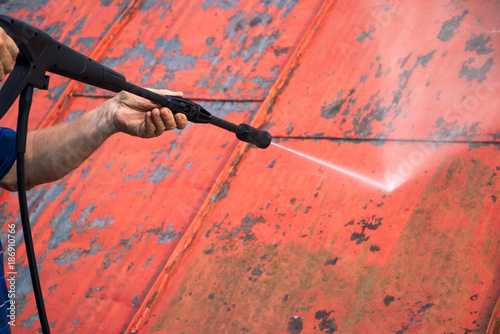 Man is washing the roof with a high pressure washer. Worker cleaning a red metal sheet roof by water. Detail  photo