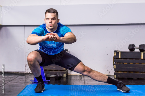 Fit young man doing side lunges at the gym