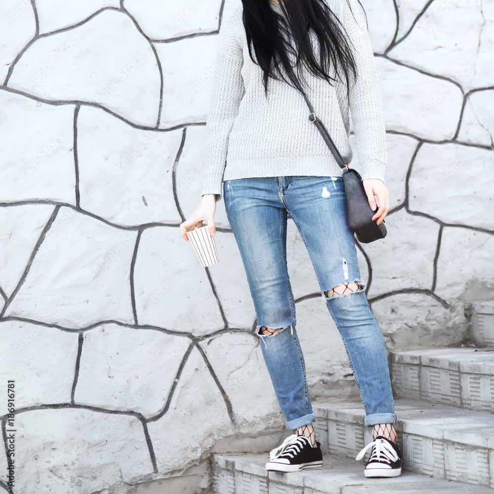 Fashionable woman sitting on stairs wearing ripped jeans with sneakers.