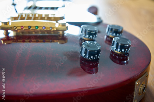 Tone And Volume Knobs On a Shiny Wine Red Guitar With Golden Hardware Placed On A Wooden Table 