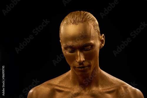 man in gold paint portrait. guy looks down with eyelids lowered almost closed eyes on black background