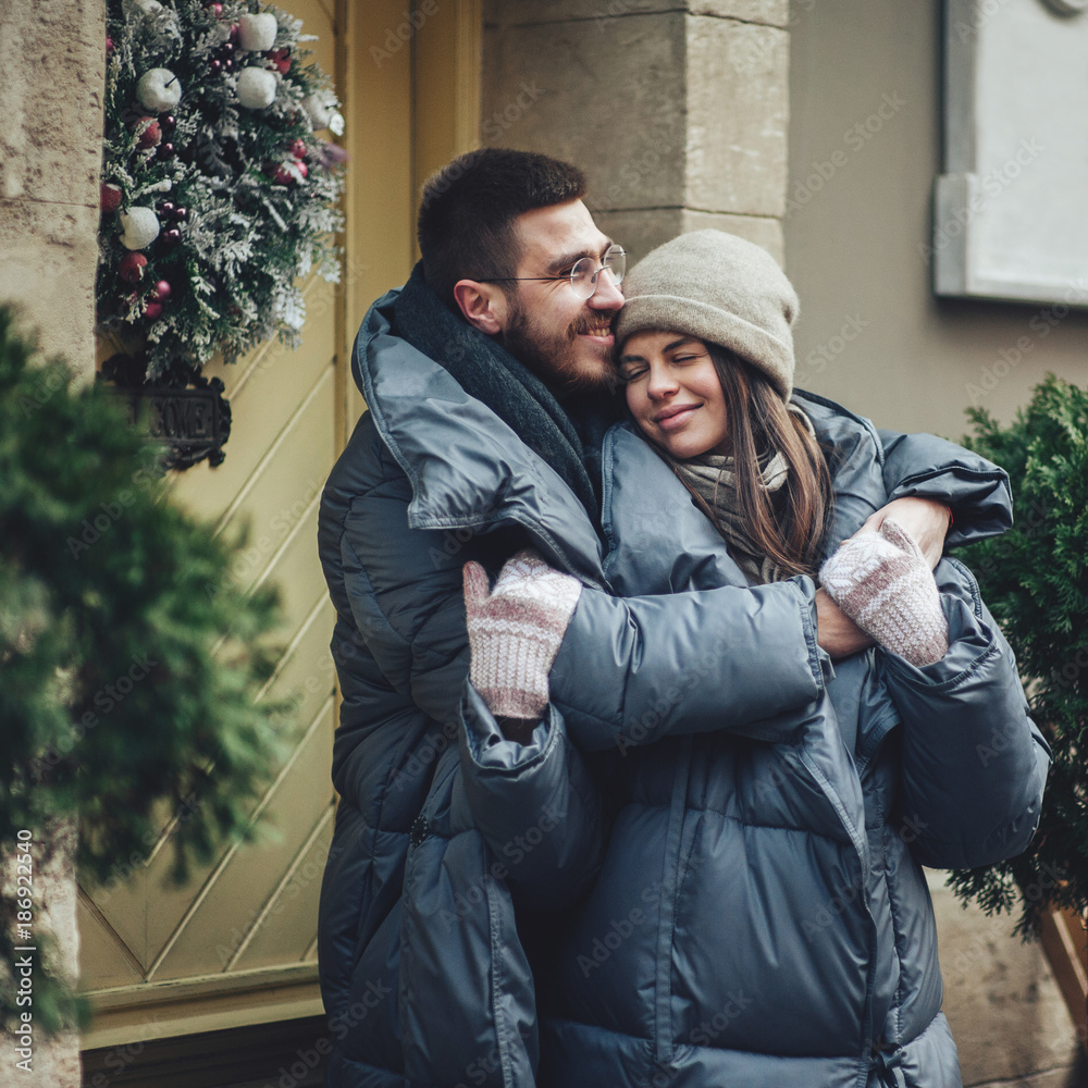 Fototapeta premium Couple has fun and laughs. kiss. Young hipster couple hugging each other in winter park. Winter love story, a beautiful stylish young couple. Winter fashion concept with boyfriend and girlfriend.