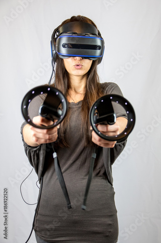 Junge Frau mit Virtual Reality Datenbrille zielt mit  zwei Controllern photo