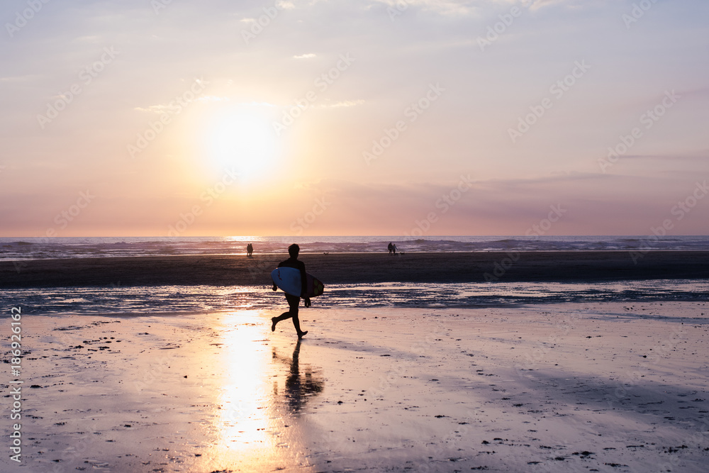 Surfer running towards water at sunset
