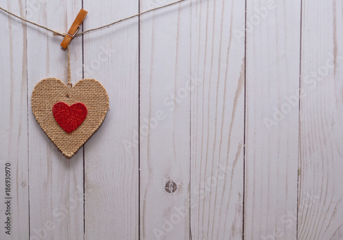 A single brown heart with a smaller red heart in it;s center hanging on a line in front of a white wooden fence