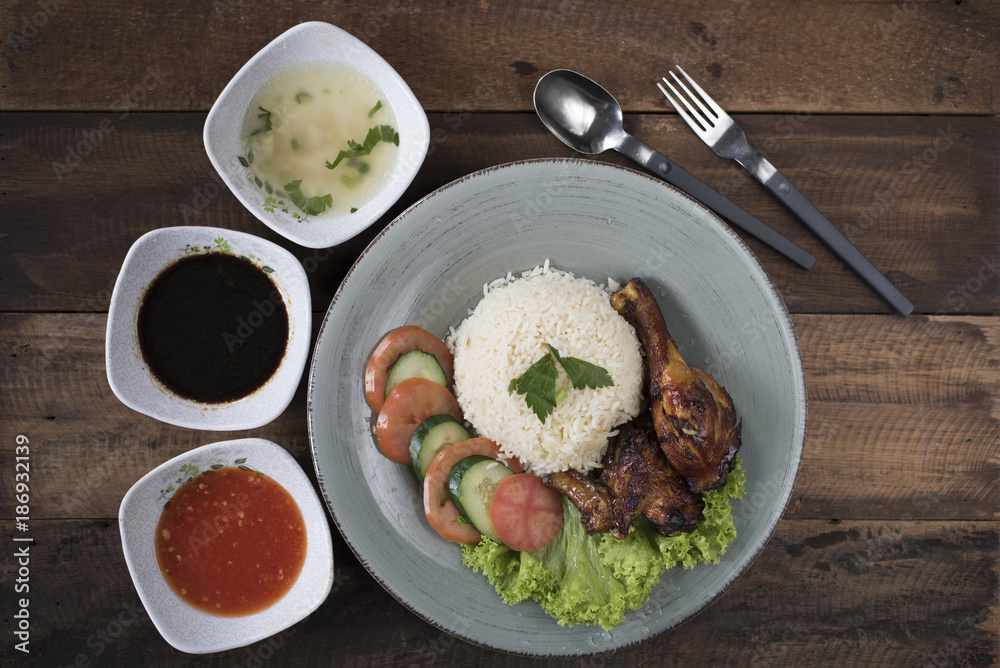 Popular Malaysian dish Nasi Ayam or chicken rice with baked chicken pieces, tomato, cucumber, salad, soup, soy sauce and chili sauce.