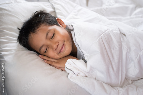 boy sleeping with smile face on white bed sheet and pillow.boy fall asleep with smiling face having sweet dream.sleep concept