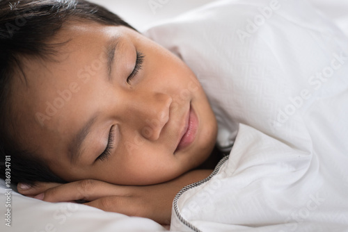boy sleeping with smile face on white bed sheet and pillow.boy fall asleep with smiling face having sweet dream.sleep concept