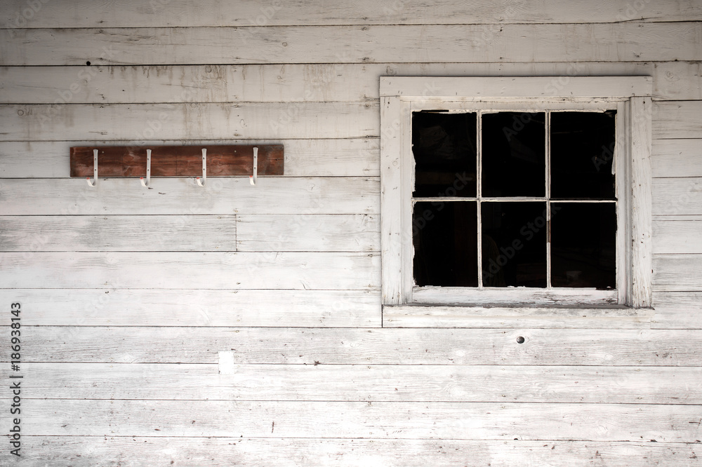 Four old coat hooks hanging on a faded white washed wood plank exterior wall beside a peeling six paned window Four old coat hooks hanging on a faded white washed wood plank exterior wall beside a peeling six paned window