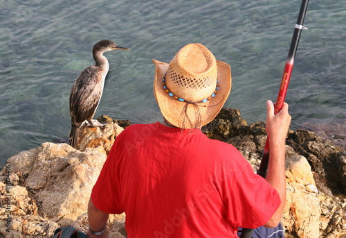 Man fishing in the sea with cormorant waiting for his catch. photo