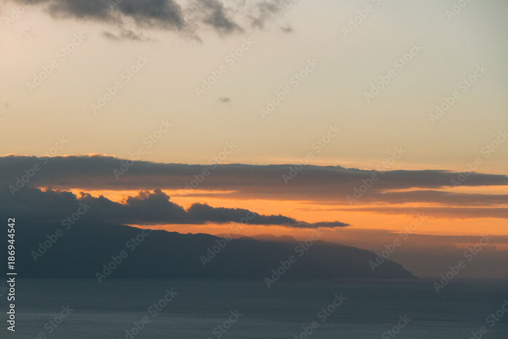 Sunset light behind clouds above mountains and ocean