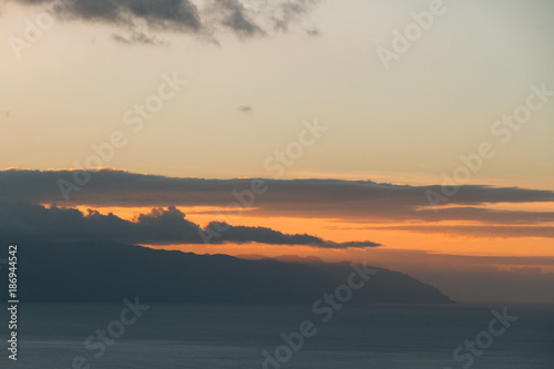 Sunset light behind clouds above mountains and ocean