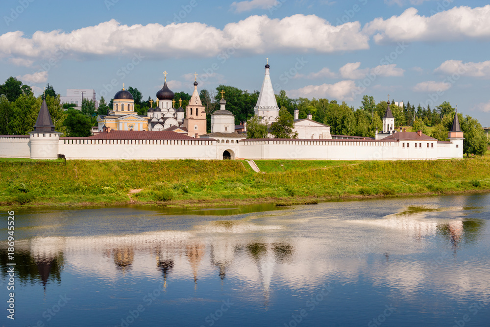 View on ancient white-stone Convent of the Dormition built in 16 century on Volga River bank with reflection in water. Staritsa, Tverskoy region, Russia.