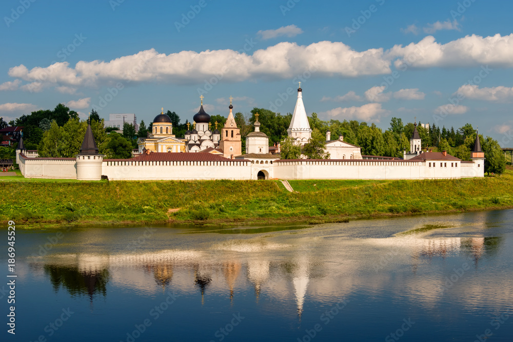 View on ancient white-stone Convent of the Dormition built in 16 century on Volga River bank with reflection in water. Staritsa, Tverskoy region, Russia.