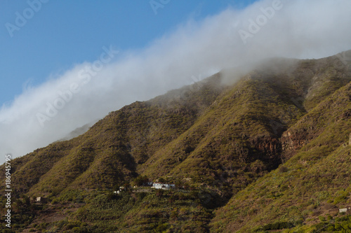 Houses on hillside of green mountain covered in fog
