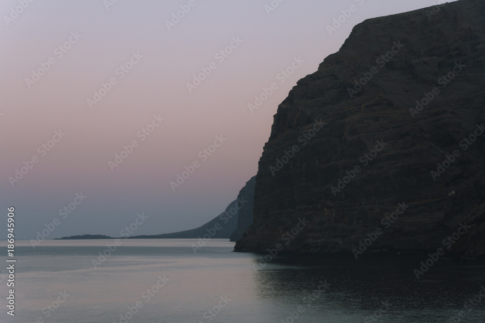 Calm ocean water and big cliffs in dusk before sunrise