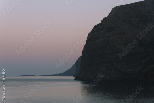 Calm ocean water and big cliffs in dusk before sunrise