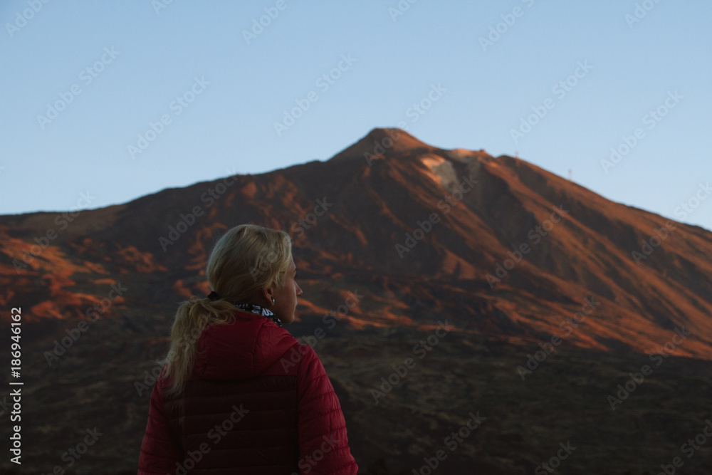 Woman walking with sunrise light on volcano in desert landscape