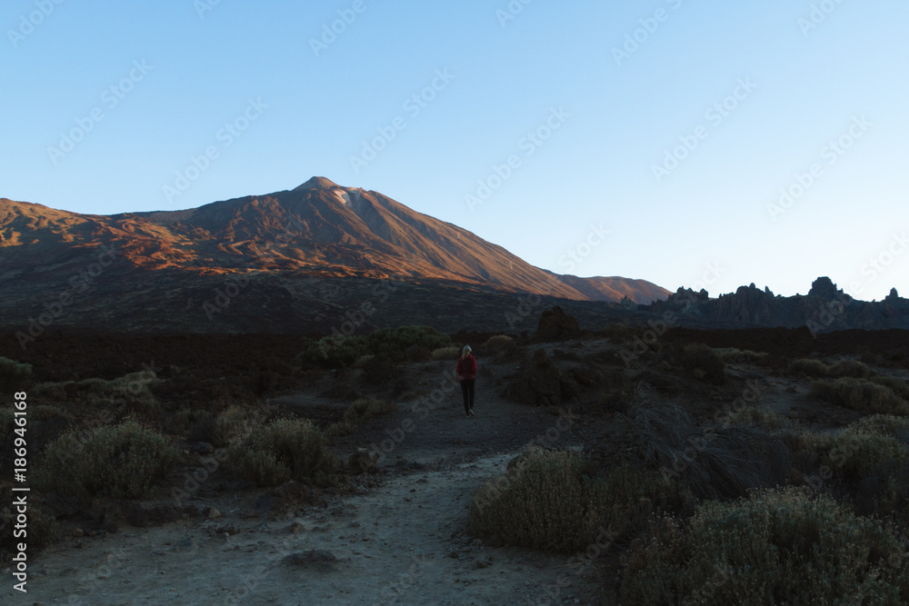 Woman walking with sunrise light on volcano in desert landscape Woman walking with sunrise light on volcano in desert landscape