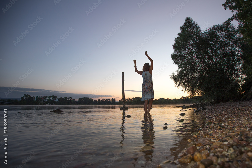 Junge attraktive Latina in weißem Kleid steht im Sonnenaufgang im Fluß