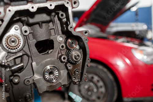 Selective focus. Engine Block on a repair stand with Piston and Connecting Rod of Automotive technology. Blurred red car on background. Interior of a car repair shop.