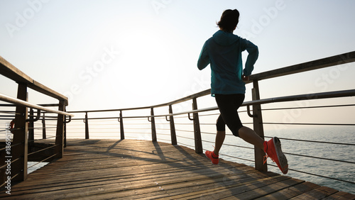 sporty fitness female runner running on seaside boardwalk during sunrise