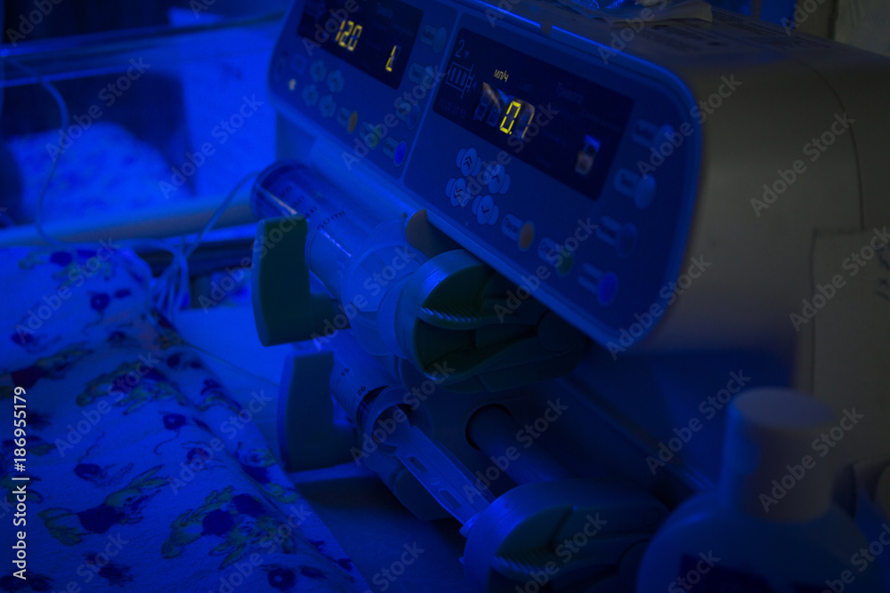 Newborn baby under blue UV light for on infant warmer in neonatal