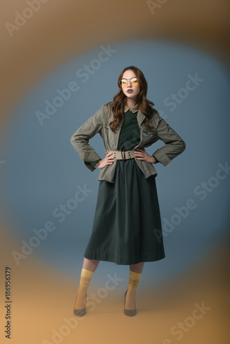 beautiful model posing in autumn outfit and yellow sunglasses, isolated on grey with orange filter