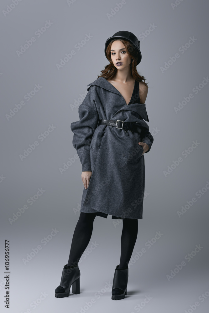 beautiful woman posing in trendy autumn coat and military helmet, isolated on grey beautiful woman posing in trendy autumn coat and military helmet, isolated on grey