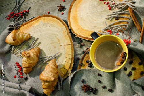 croissants and a cup of coffee on a wooden surface among a woolen blanket and red berries. Autumn motive