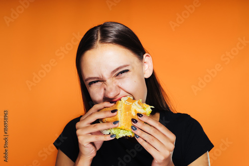 a young girl in a black T-shirt is very hungry, eagerly eats a harmful burger