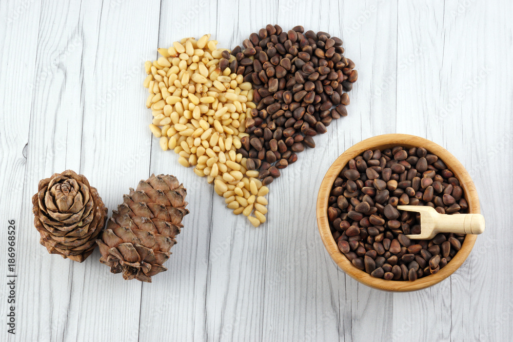Top view of pine nuts laid out in the form of a heart on a wooden table, next to a bamboo bowl with nuts and cedar cones Top view of pine nuts laid out in the form of a heart on a wooden table, next to a bamboo bowl with nuts and cedar cones