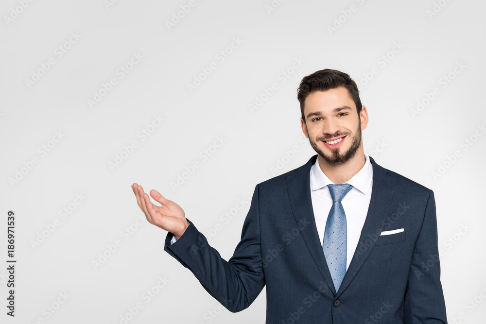 handsome young businessman showing copy space and smiling at camera isolated on grey handsome young businessman showing copy space and smiling at camera isolated on grey