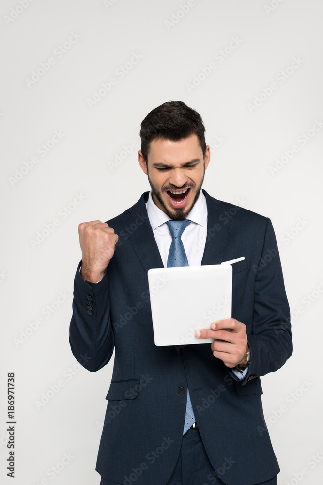 triumphing young businessman holding digital tablet isolated on grey triumphing young businessman holding digital tablet isolated on grey