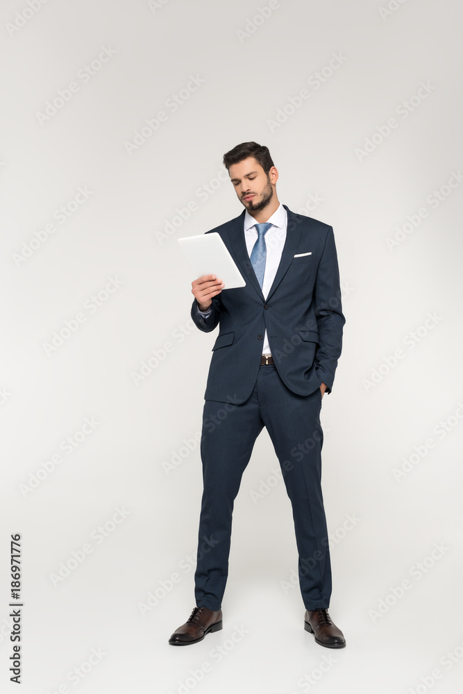 full length view of confident young businessman using digital tablet isolated on grey full length view of confident young businessman using digital tablet isolated on grey