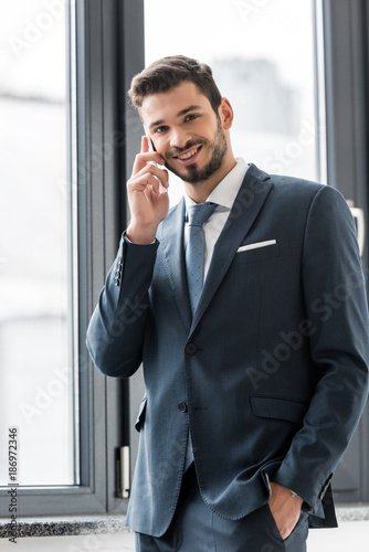 young businessman talking on smartphone and smiling at camera in office