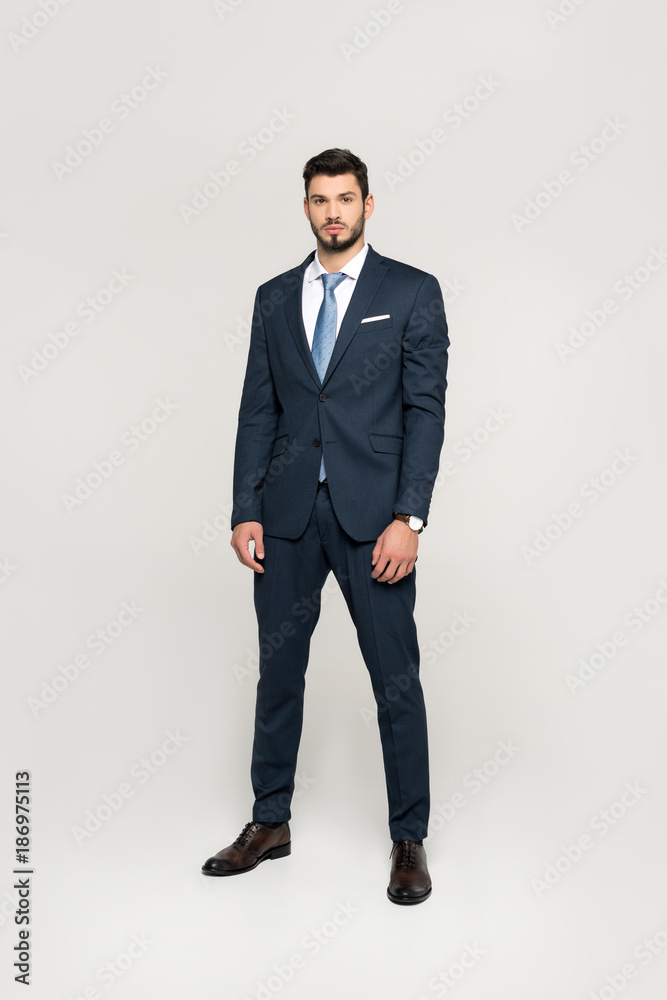 full length view of stylish handsome young businessman looking at camera isolated on grey full length view of stylish handsome young businessman looking at camera isolated on grey
