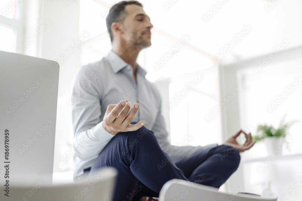 Businessman sitting on table in office practicing yoga Businessman sitting on table in office practicing yoga