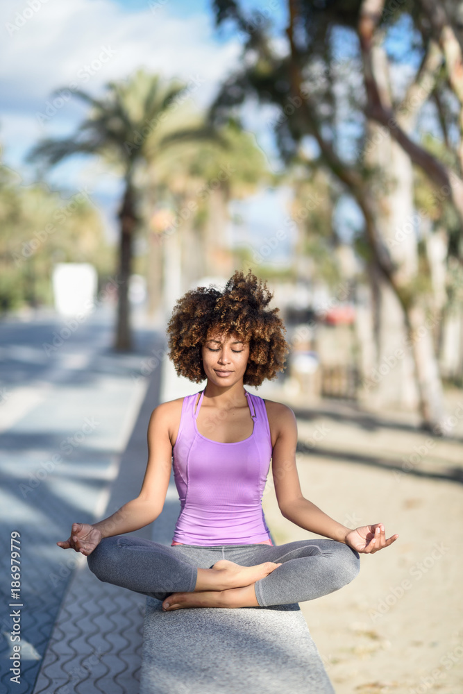 Black woman, afro hairstyle, in lotus pose with eyes closed in the beach