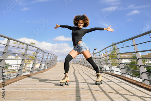 Afro hairstyle woman on roller skates riding outdoors on urban bridge